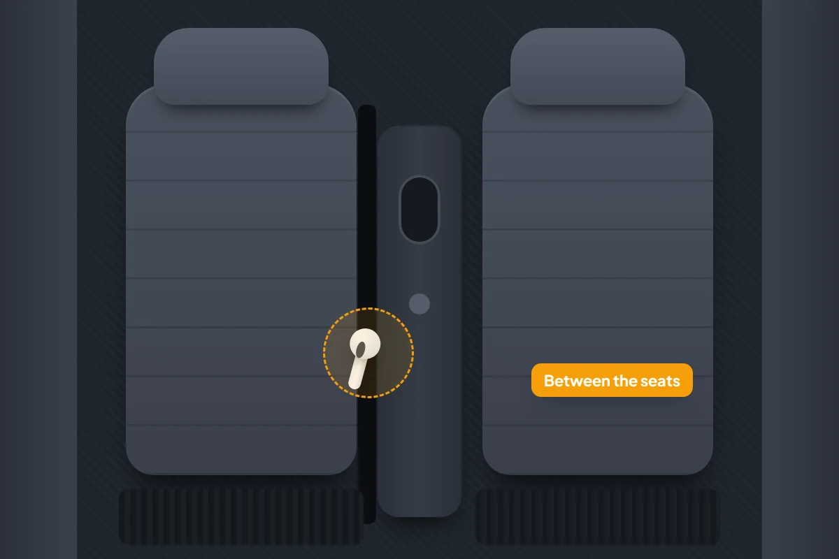 Top-down view of two car front seats with an earbud caught in the gap between a seat and the centre console