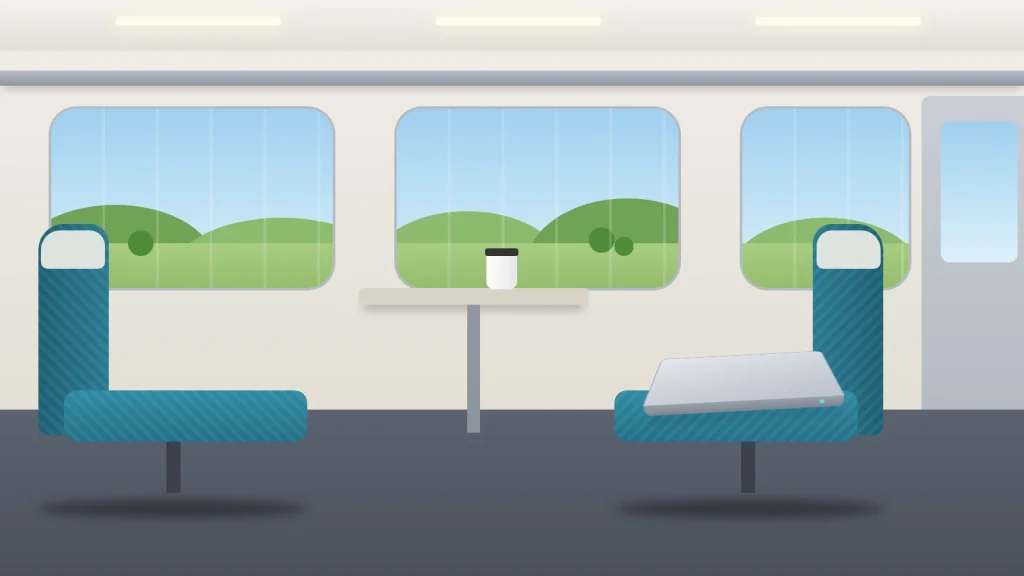 A train carriage with countryside through the windows and a closed laptop left behind on an empty seat