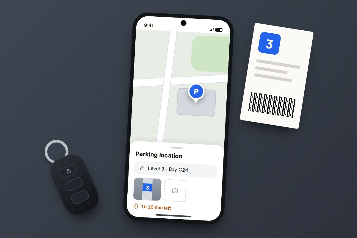 A phone on a car seat showing a parking note reading Level 3, bay C24, a photo and time left, beside a key fob and ticket