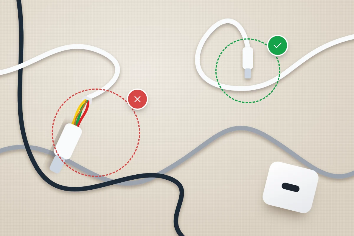Flat-lay of tangled charging cables on a desk, one with a split, frayed end marked with a red cross and a clean one ticked