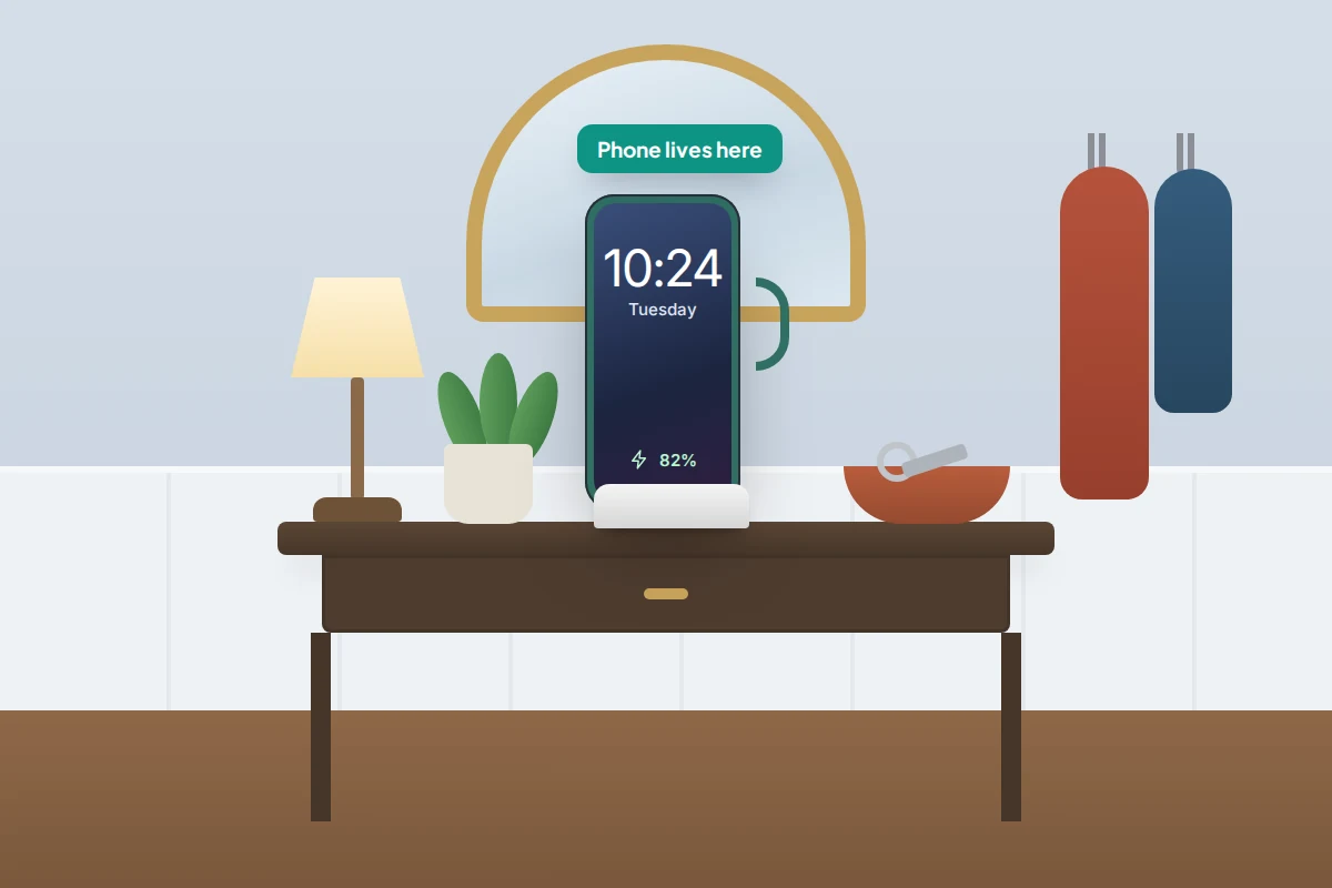 A hallway table with a phone standing in a charging dock beside a lamp, a key bowl and a small plant