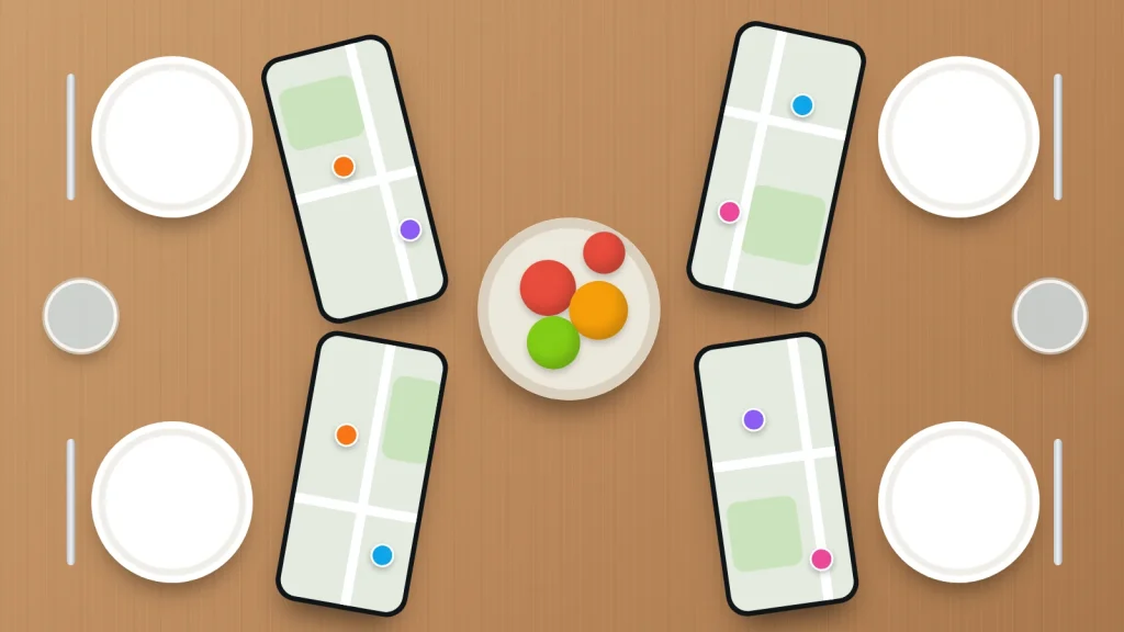 A family dinner table seen from above, with four phones beside the plates each showing a map with family members' dots