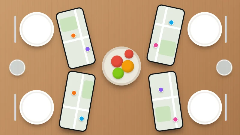 A family dinner table seen from above, with four phones beside the plates each showing a map with family members' dots