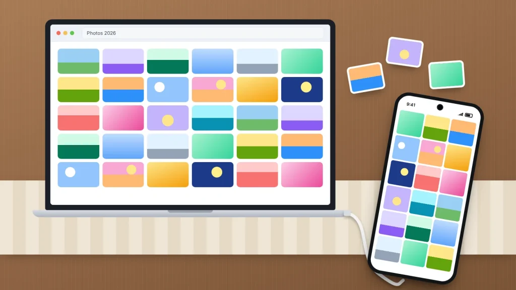 A laptop showing a grid of photos on a wooden dining table, connected by a white cable to a phone full of photos