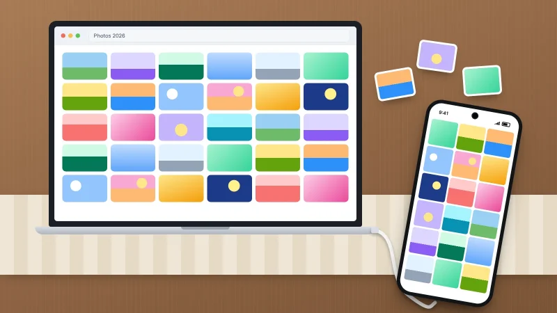 A laptop showing a grid of photos on a wooden dining table, connected by a white cable to a phone full of photos