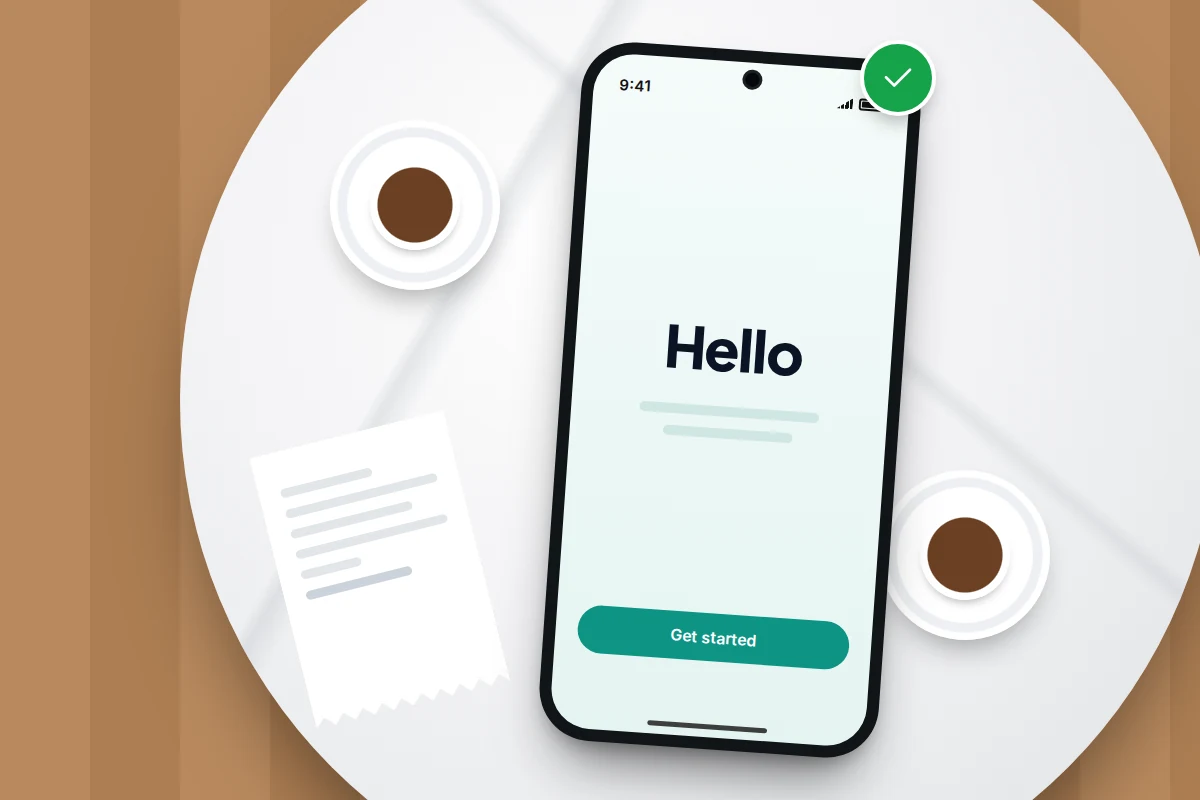 A phone on a cafe table showing a welcome setup screen with a green tick, between two cups and a paper receipt